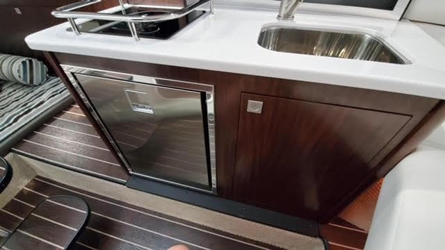2019 Monterey 295 yacht interior with kitchenette, featuring sink, stove, and wood cabinetry.
