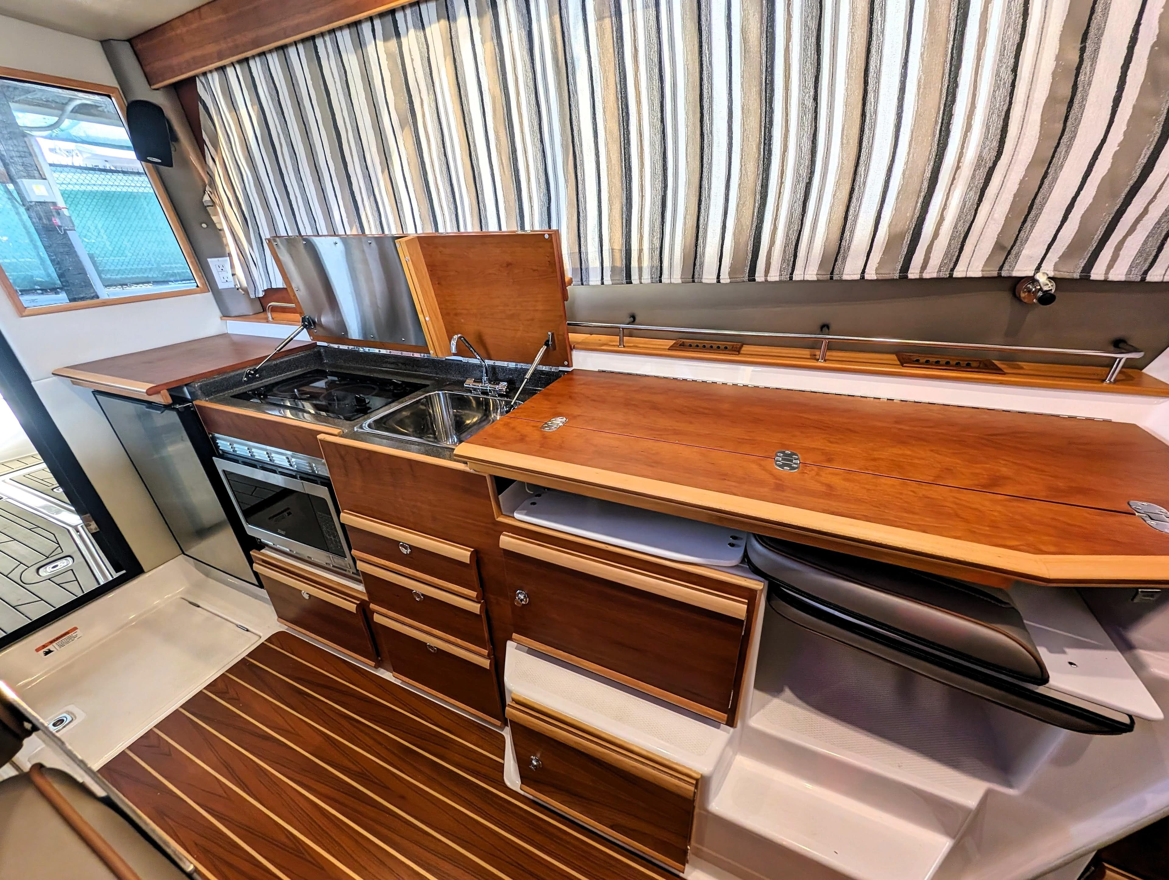 2022 Cutwater C-32 Coupe LE kitchen with wood cabinetry, stove, sink, and striped curtains.